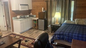 Een kleine kamer met een kitchenette, een bed, een bureau en een stoel.