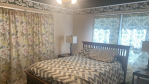 Een slaapkamer met een houten bed, bloemen gordijnen en een raam met behang.