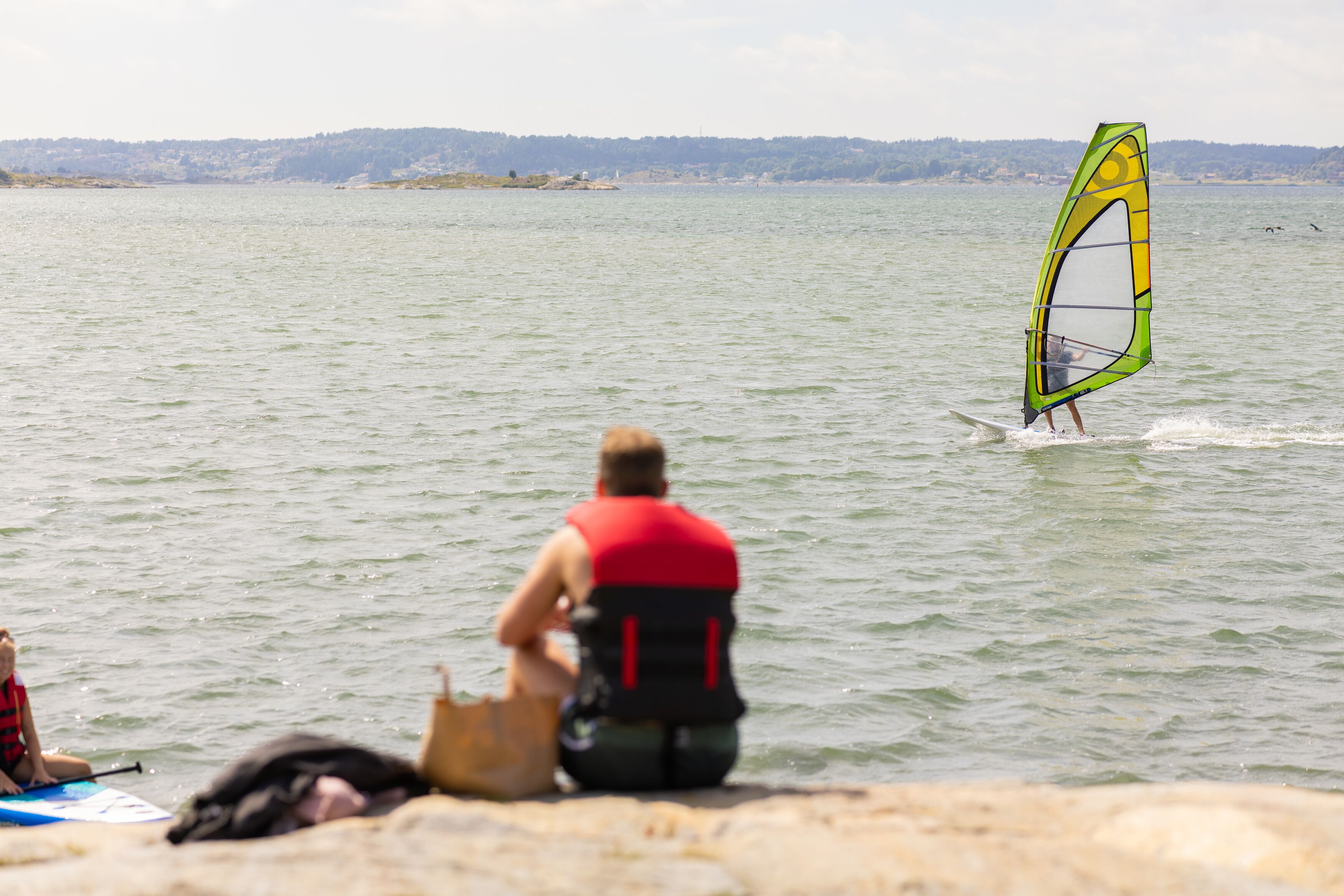 A person windsurfing on a lake with a distant shoreline.