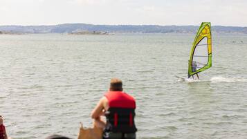 Une personne pratiquant la planche à voile sur un lac, avec une côte visible au loin.