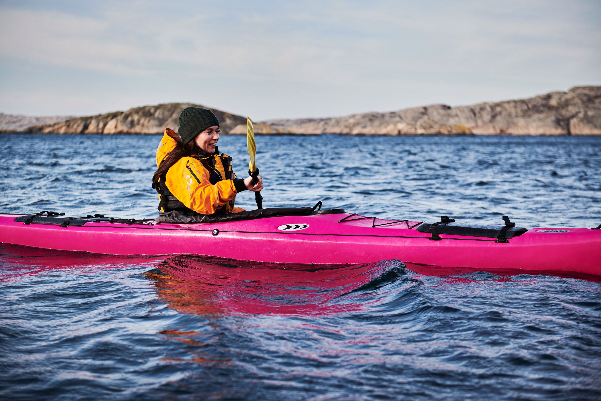 A person kayaking on a body of water with rocky cliffs in the background.