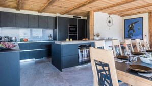 Een moderne keuken met donkere kastjes, een centraal eiland en een eethoek met houten stoelen en een tafel voor twee personen.