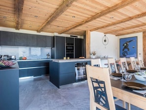 A modern kitchen with dark cabinetry, a central island, and a dining area with wooden chairs and a table set for two.