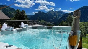 Een hottub met champagnefles en een glas, omgeven door bergen en een heldere lucht.