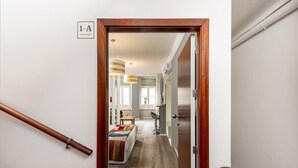 Un pasillo que conduce a un dormitorio con una puerta de madera, una mesita con una manta colorida y una ventana con cortinas.