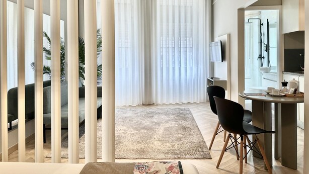 Una habitación de hotel moderna con un ventanal grande, televisor de pantalla plana, zona de comedor y cabina de ducha.
