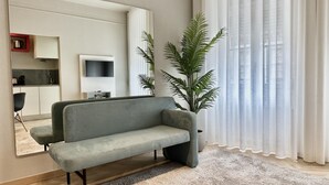Una sala de estar con un sofá gris, un espejo grande, un televisor y una planta en maceta.