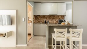 A modern kitchen with a granite countertop, white cabinets, and a herringbone backsplash. There are two white bar stools and a microwave on the counter. - Capela 2 in Oporto With 1 Bathrooms (Porto)