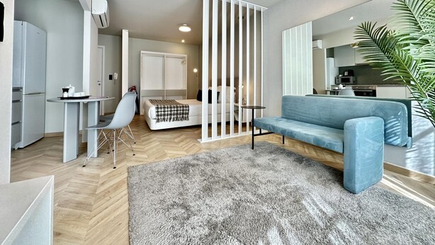A modern living room with a sofa, a small table, a chair, a bed, and a kitchen area in the background. - Capela 2 in Oporto With 1 Bathrooms (Porto)
