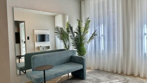 A modern living room with a grey sofa, a small round table, a large mirror, and a potted plant. - Capela 2 in Oporto With 1 Bathrooms (Porto)