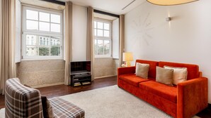 A living room with a red sofa, a plaid armchair, a TV stand, and large windows with curtains. - Torre 1 in Oporto With 1 Bathrooms (Porto)