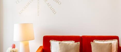 A red sofa with two pillows, a table with a lamp, and a wall with text in multiple languages.