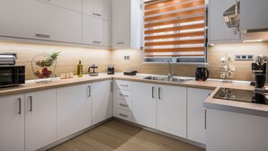 A modern kitchen with white cabinets, a wooden countertop, a built-in oven, and a window with blinds. - Villa Cataleya : A Spacious, Private Oasis with a Pool Near the Beach (Chania)