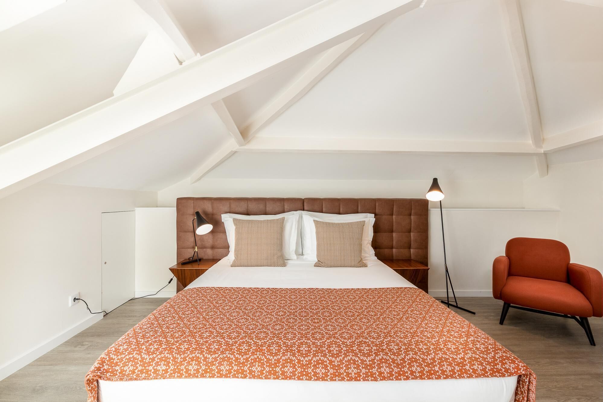 A bedroom with a bed, a brown headboard, a red chair, and a floor lamp.