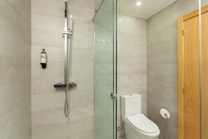 Un baño moderno con ducha separada por vidrio, inodoro y puerta de madera.