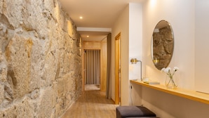 A hallway with a stone wall, wooden bench, and a mirror on the wall. - Ribeira Gaia 2 in Vila Nova de Gaia (Vila Nova de Gaia)