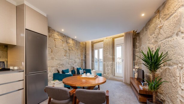 A modern kitchen with a built-in refrigerator, a dining area with a wooden table and chairs, and a stone wall. - Ribeira Gaia 2 in Vila Nova de Gaia (Vila Nova de Gaia)