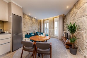 A modern kitchen with a built-in refrigerator, a dining area with a wooden table and chairs, and a stone wall.