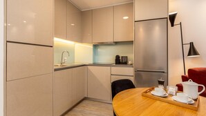 A modern kitchen with a wooden dining table set for breakfast, a refrigerator, and a coffee machine. - Ribeira Gaia 3 in Vila Nova de Gaia (Vila Nova de Gaia)