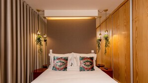 A hotel room with a large bed, two decorative pillows, a wooden wardrobe, and wall-mounted lights. - Ribeira Gaia 3 in Vila Nova de Gaia (Vila Nova de Gaia)