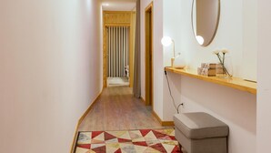 A hallway with a geometric patterned rug, a bench, a mirror, and a shelf with decorative items. - Ribeira Gaia 3 in Vila Nova de Gaia (Vila Nova de Gaia)