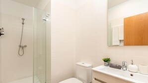 Une salle de bain moderne avec une douche à parois de verre, des toilettes blanches et un meuble-lavabo doté d’un miroir, d’un évier et d’une petite plante.