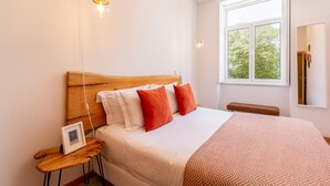 Une chambre à coucher avec une tête de lit en bois, une grande fenêtre et une table de chevet sur laquelle est posé un cadre photo.