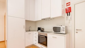 Une cuisine compacte avec des meubles blancs, un four à micro-ondes, une machine à café et un petit four.