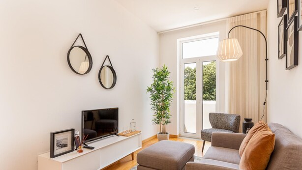 A modern living room with a flat-screen TV, a white console table, a grey sofa, and a large window with a view of greenery. - Cosy 5 in Oporto With 1 Bedrooms and 1 Bathrooms (Porto)