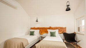 Een slaapkamer met twee eenpersoonsbedden, een houten hoofdbord, een klein tafeltje, een zwarte stoel en een raam.