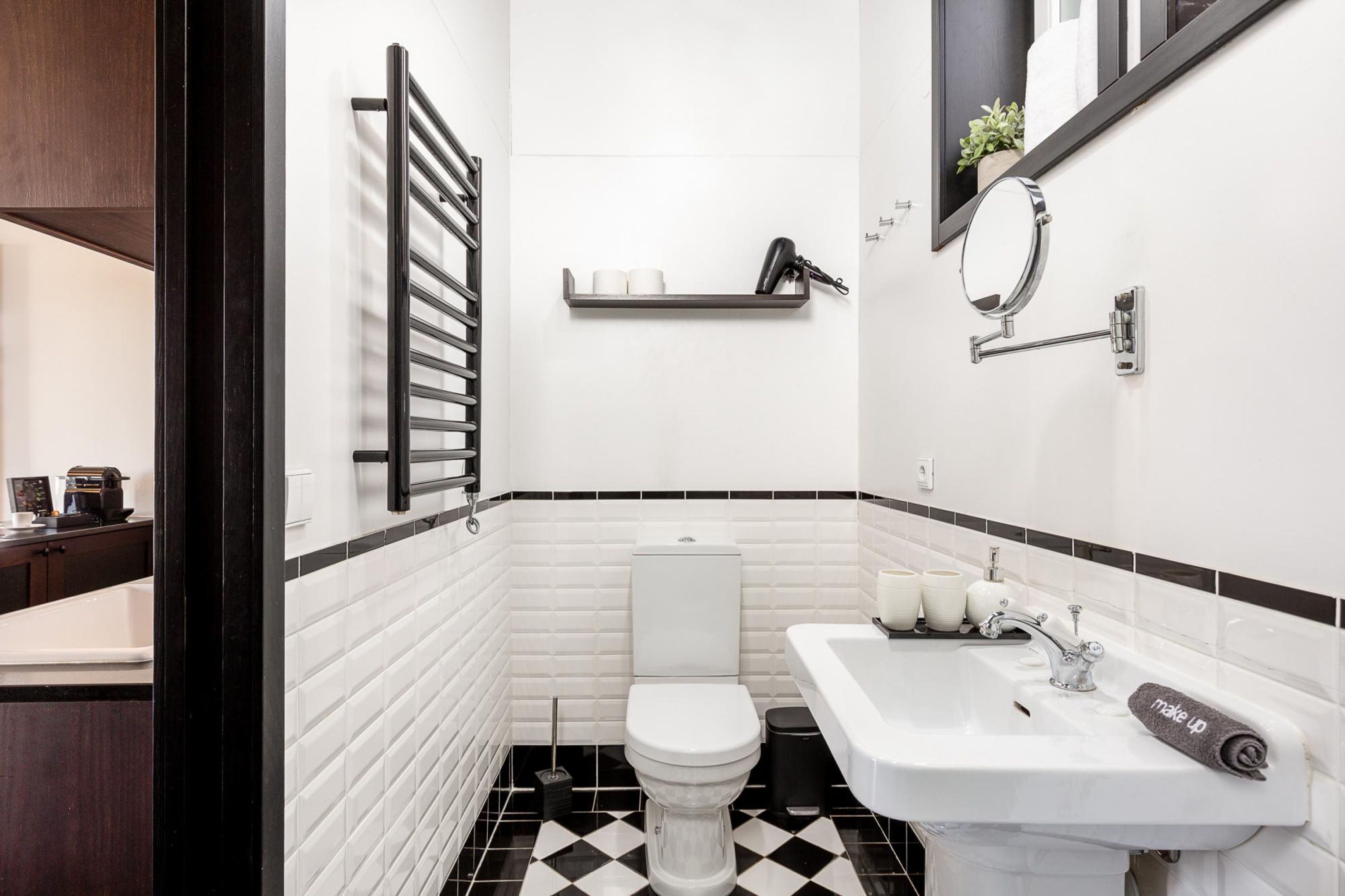 A modern bathroom with a black and white tiled floor, a white toilet, a sink with a mirror, and a towel rack.