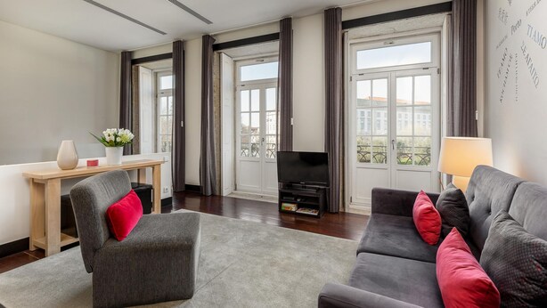 Un saló modern amb un sofà gris, una cadira vermella, un televisor de pantalla plana i una taula de fusta amb un ram de flors.