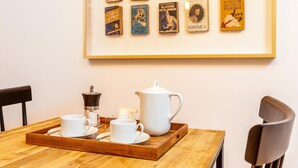 Ett matbord med ett bricka som innehåller en kaffekanna, koppar och fat. En inramad samling böcker hänger på väggen bakom.