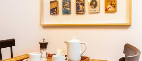 A dining table with a tray holding a coffee pot, cups, and saucers. A framed collection of books is displayed on the wall behind.