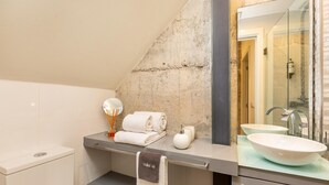 Une salle de bain au design moderne, comprenant une douche à parois de verre, un grand miroir et un plan de toilette avec un lavabo sur colonne.