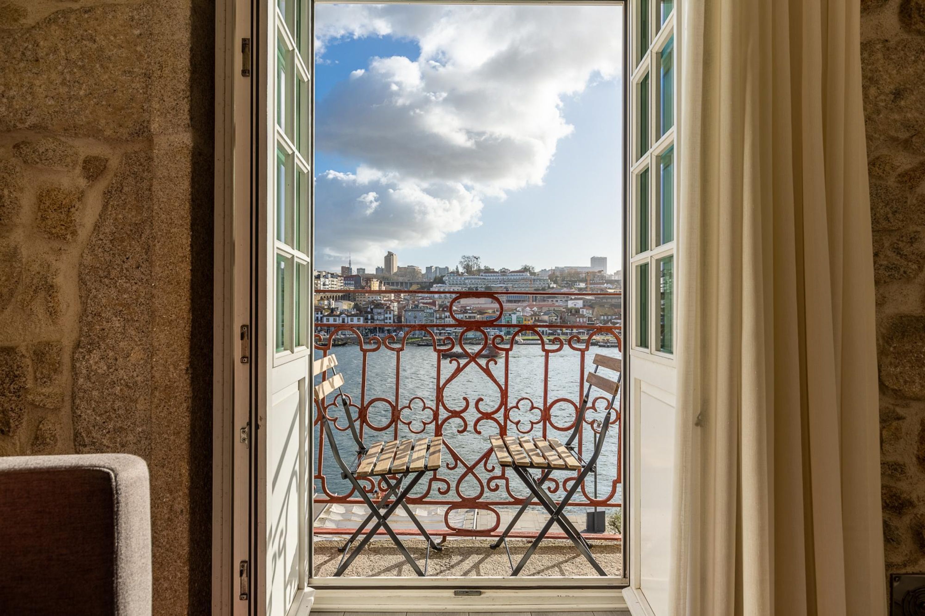 Un balcón con barandilla de metal, vista a un cuerpo de agua y un paisaje urbano al fondo.