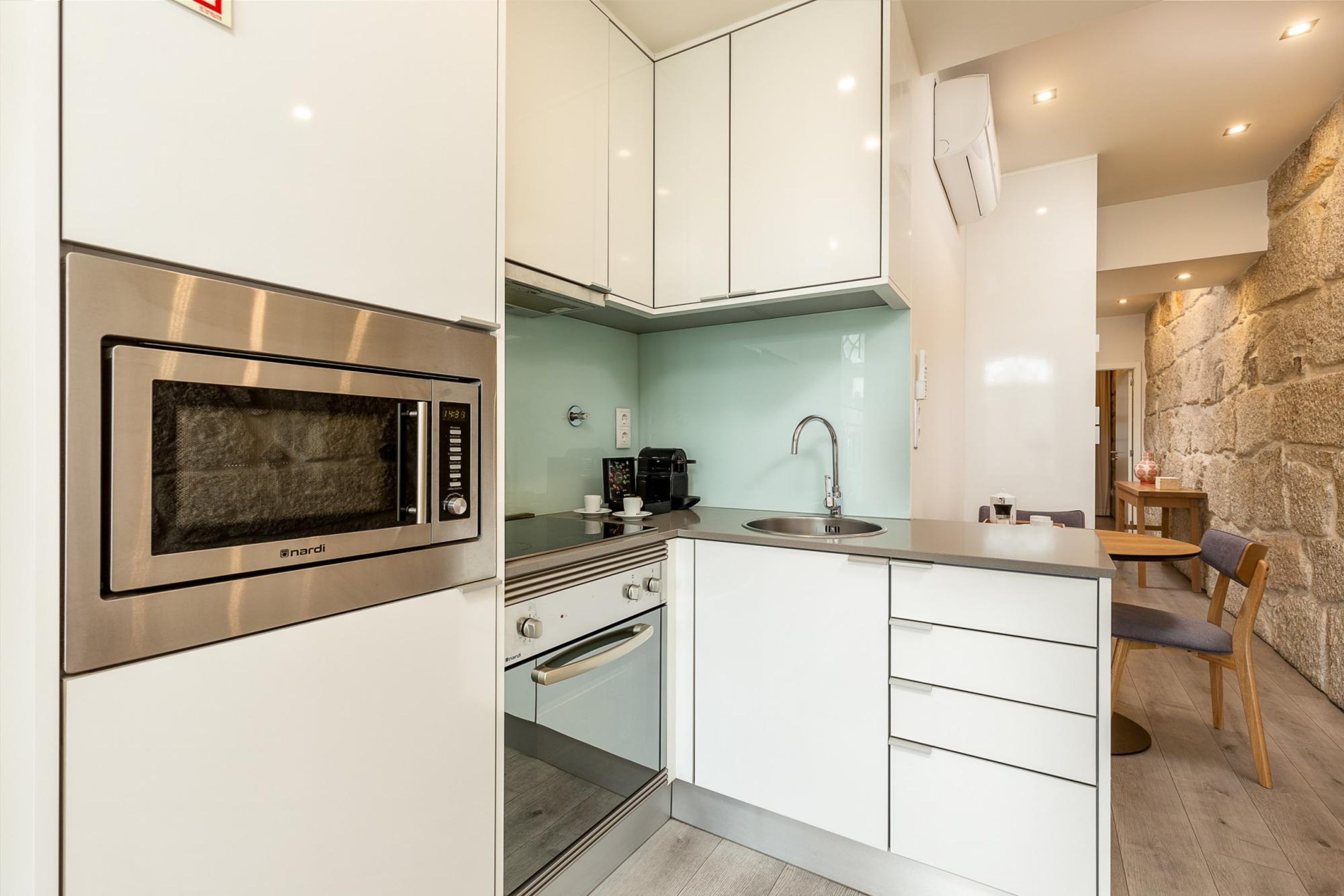 A modern kitchen with white cabinets, a built-in oven, a microwave, a sink, and a stone accent wall.