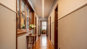 A hallway with wooden flooring, a vase with flowers on a table, and a chair in the distance. - Santa Catarina 1D in Oporto (Porto)