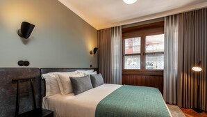 A hotel room with a bed, a bedside table, a lamp, a window with curtains, and a view of buildings outside. - Santa Catarina 1D in Oporto (Porto)