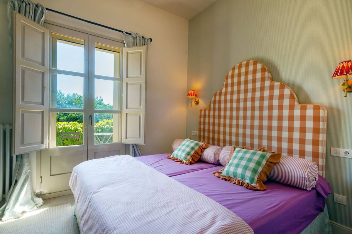 A bedroom with a large bed, checkered headboard, and a window with curtains.