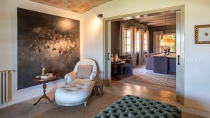 A spacious living room with a large abstract painting, a plush armchair, a green ottoman, and a view into the dining area. - CAN CASI HOUSE (Parlava)