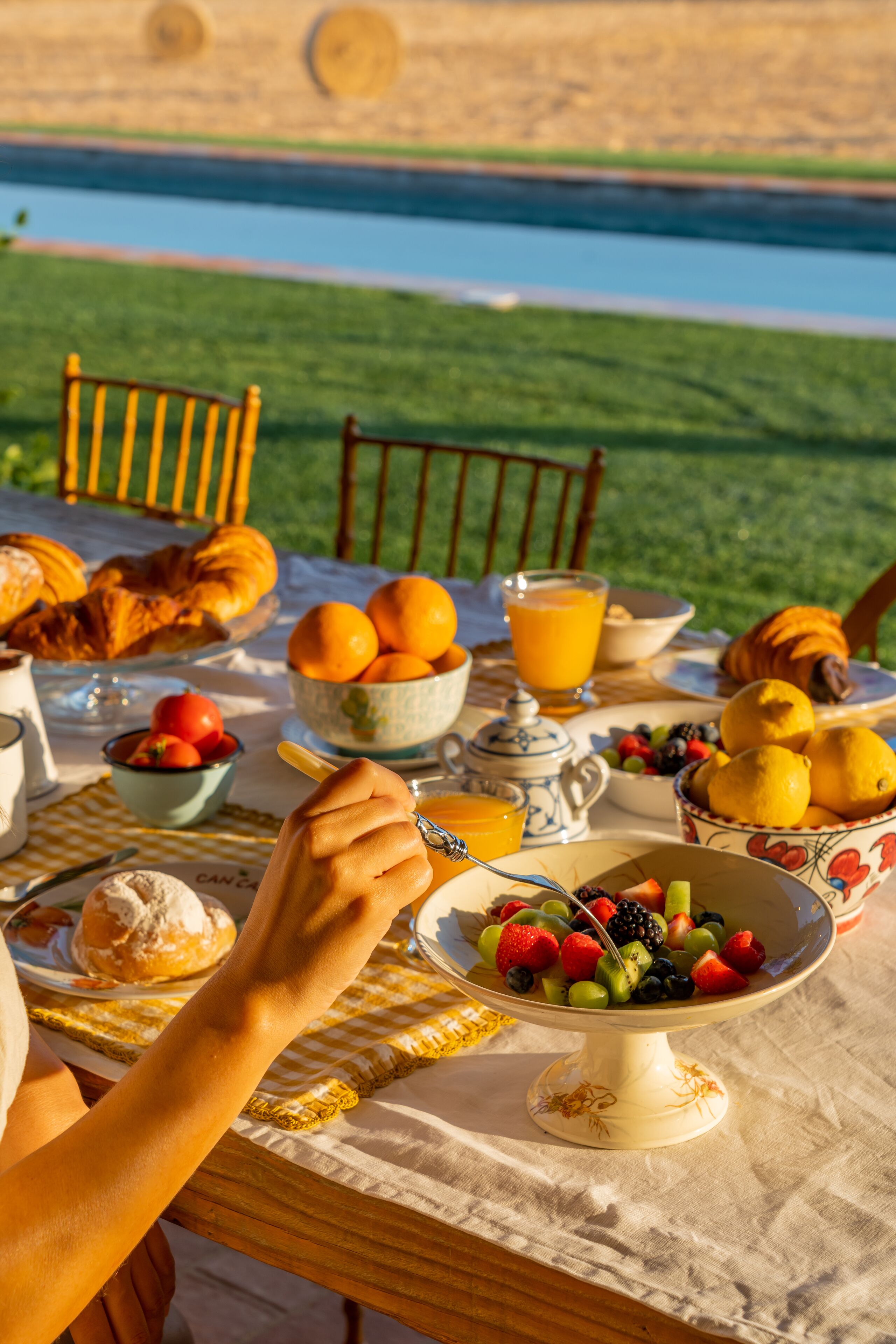 Una mesa de desayuno con croissants, naranjas y un bol de fruta.