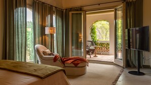 A bedroom with a bed, a chair, a TV, and a sliding glass door leading to an outdoor area with a table and chairs. - CAN CASI HOUSE (Parlava)