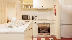 Una cocina compacta con armarios blancos, un microondas, un horno y un refrigerador.