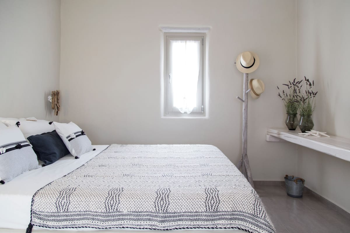 A bedroom with a bed, pillows, a bedside table, a window, and a floor lamp.