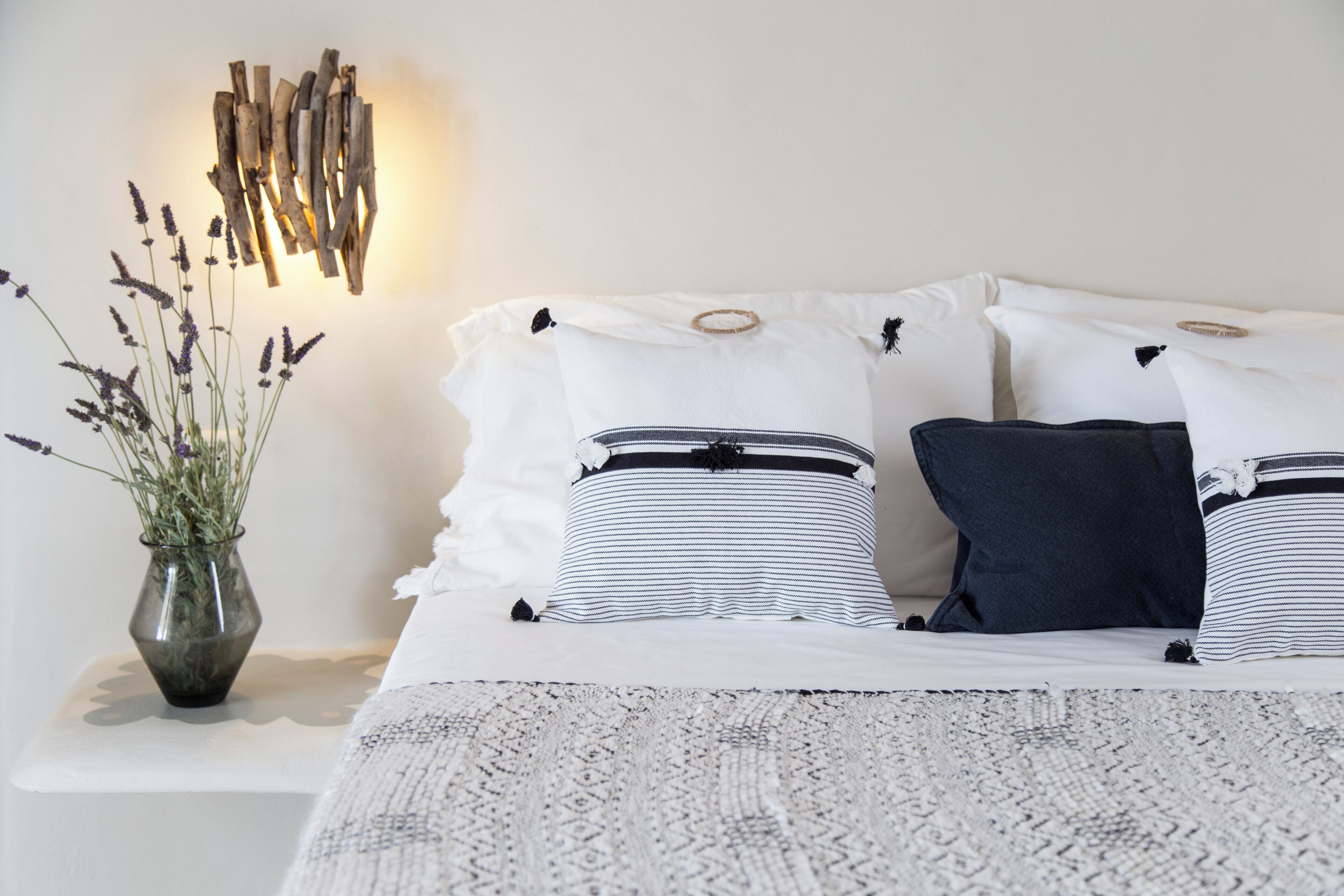 A neatly arranged bedroom with a bed, pillows, a bedside table, and a wall-mounted light fixture.