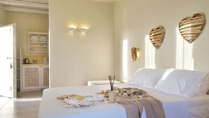 Una cama bien hecha con un edredón color beige, una mesita de noche con un libro, un florero con velas y una decoración con forma de corazón en la pared.