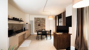 A compact kitchen with a dining area, a stone accent wall, and a TV mounted on the wall. - Domus Acaja-Elegant Apartment in the Historic Center-Fully Equipped Kitchen (Pinerolo)