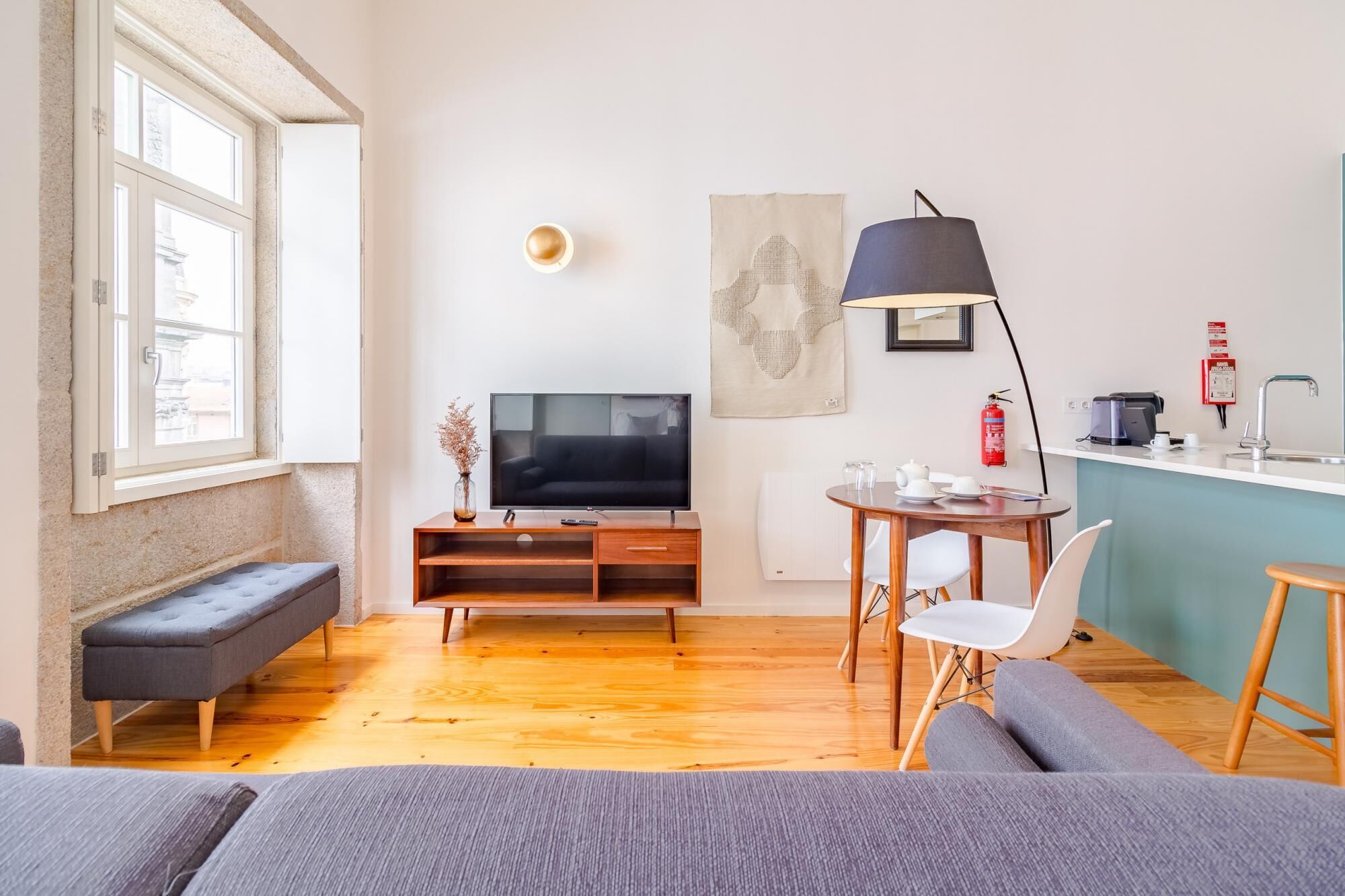 Una sala moderna con una televisión de pantalla plana, un banco, un sofá, una mesa de comedor con sillas, una máquina de café y un extintor.
