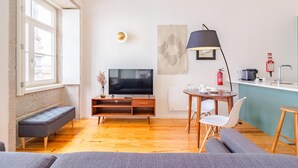 A modern living room with a flat-screen TV, a bench, a sofa, a dining table with chairs, a coffee machine, and a fire extinguisher. - Tower 5F in Oporto With 1 Bathrooms (Porto)